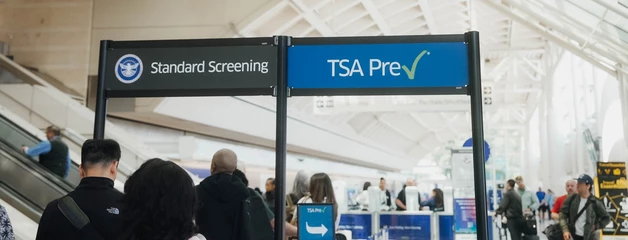 Airport terminal with TSA PreCheck sign and passengers queuing at security checkpoint