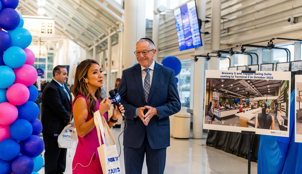 A dignitary with a woman in pink dress at an event with blue and pink balloon decorations.
