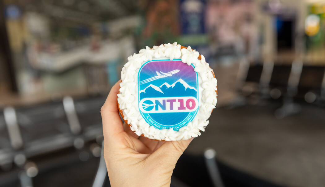 Hand holding a cupcake with white frosting and blue "ONT10" logo decoration