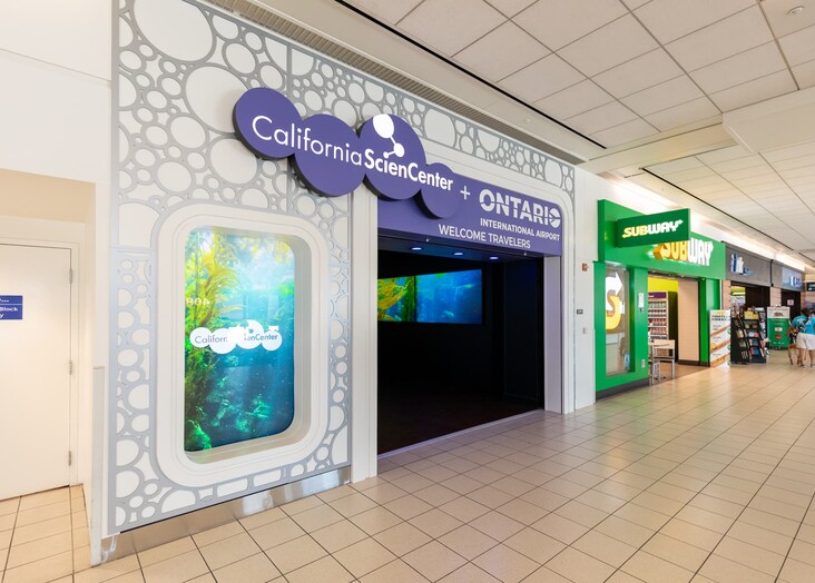 Colorful storefront display with a white decorative panel and digital screens in a shopping mall hallway.